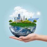 Hand holding small earth model with city and greenery.