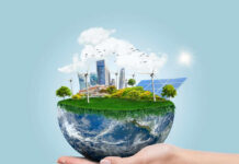 Hand holding small earth model with city and greenery.