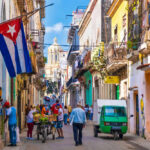 Colorful street scene with Cuban flag and people.