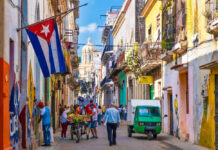 Colorful street scene with Cuban flag and people.