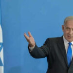 Man speaking next to Israeli flag.