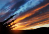 Silhouette of missiles against dramatic sunset sky.