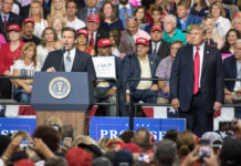 Two politicians speaking at a political rally with a large crowd in attendance