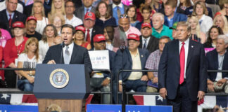 Two politicians speaking at a political rally with a large crowd in attendance