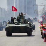 Military tanks parading down a street with a cheering crowd