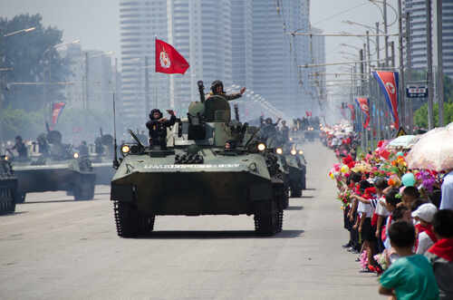 Military tanks parading down a street with a cheering crowd