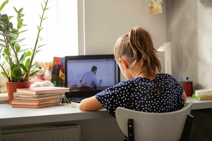 A child sitting at a desk with a laptop and books, focused on learning