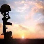 Silhouette of a soldier's helmet and rifle against a sunset