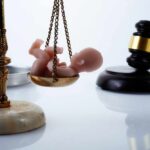 UK’s Radical Abortion Law Shocks World Scales of justice with a small baby figurine on one side and a gavel in the background