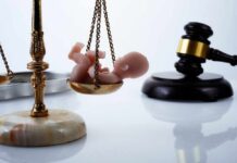 Scales of justice with a small baby figurine on one side and a gavel in the background