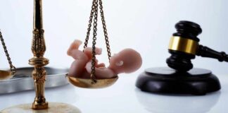 Scales of justice with a small baby figurine on one side and a gavel in the background
