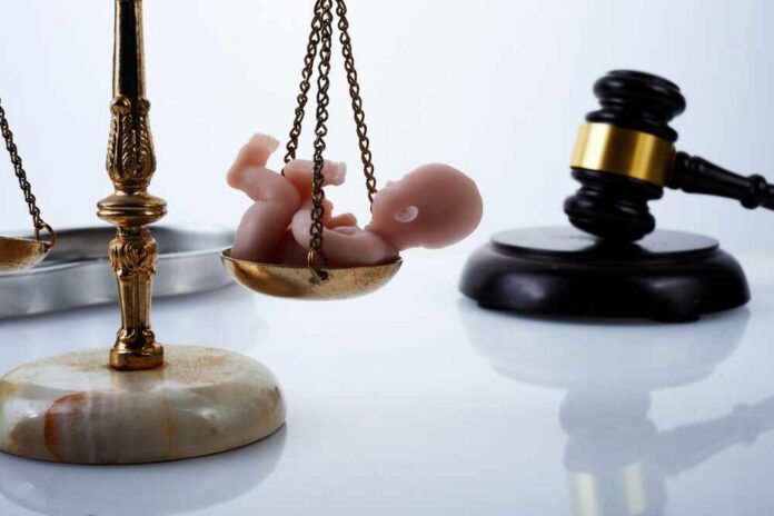 Scales of justice with a small baby figurine on one side and a gavel in the background