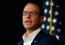 A man in a suit speaking in front of an American flag