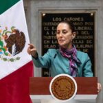 A government official delivering a speech in front of the Mexican flag