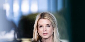 A professional woman with long blonde hair and a serious expression, wearing business attire