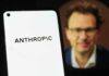 Close-up of a smartphone displaying the word 'ANTHROPIC' with a blurred portrait in the background
