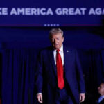 Trump’s Bold Asylum Offer Shocks Iran Man in suit walking on stage with audience background