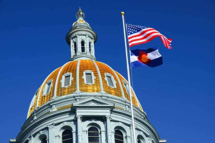 The dome of a state capitol building with flags flying against a blue sky