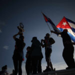 Wealthy Influencer’s Shocking Cuba Hypocrisy Exposed Silhouetted figures holding a trophy and Cuban flags during a celebration