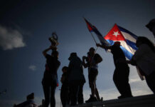 Silhouetted figures holding a trophy and Cuban flags during a celebration