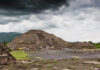 Ancient pyramid ruins under a cloudy sky with visitors