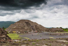 Ancient pyramid ruins under a cloudy sky with visitors