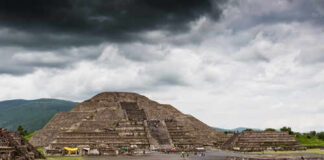 Ancient pyramid ruins under a cloudy sky with visitors