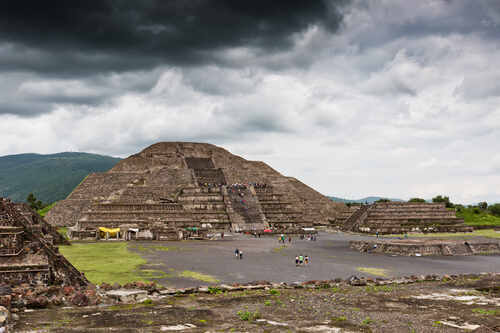 Ancient pyramid ruins under a cloudy sky with visitors