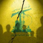 Silhouettes of individuals against a yellow wall featuring Hezbollah's emblem