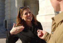 A woman in a black coat speaking animatedly during an outdoor interview