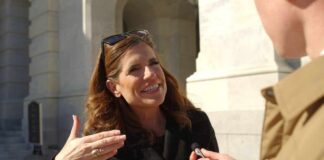 A woman in a black coat speaking animatedly during an outdoor interview