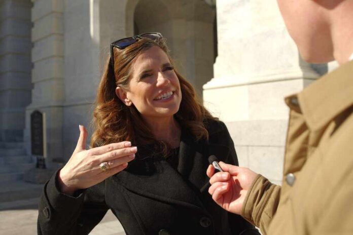 A woman in a black coat speaking animatedly during an outdoor interview