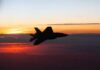 Silhouette of a fighter jet flying against a colorful sunset