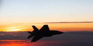 Silhouette of a fighter jet flying against a colorful sunset