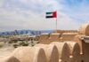 UAE flag waving atop a historic fort with a city skyline in the background