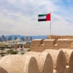 UAE flag waving atop a historic fort with a city skyline in the background