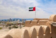 UAE flag waving atop a historic fort with a city skyline in the background
