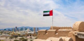 UAE flag waving atop a historic fort with a city skyline in the background