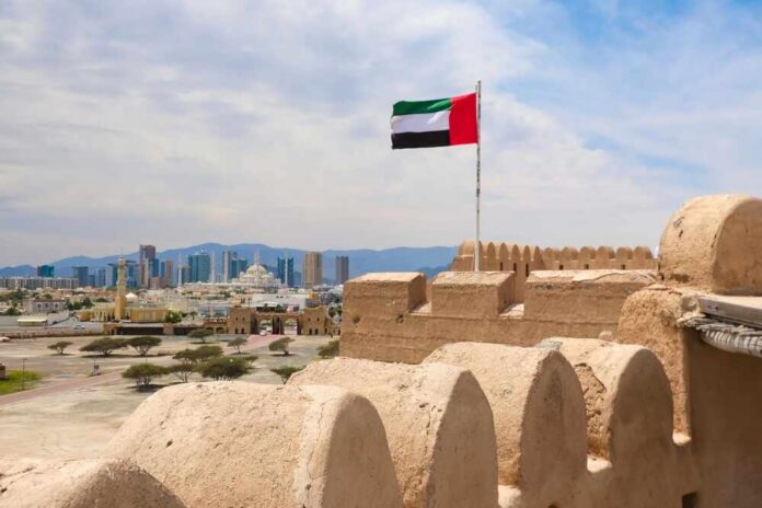 UAE flag waving atop a historic fort with a city skyline in the background