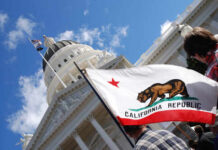 California state flag held up in front of a government building under a blue sky