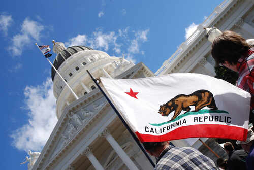 California state flag held up in front of a government building under a blue sky