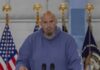 Shock Alarm: Dem Senator Calls Party ‘Anti-American’ Man in a blue hoodie speaking at a podium with U.S. flags behind