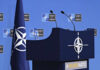 NATO Meeting: U.S. Troops On The Line? NATO podium with flags and microphones.