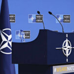 NATO Meeting: U.S. Troops On The Line? NATO podium with flags and microphones.