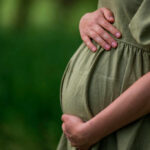 Global Baby Bust Sparks Economic Fears Pregnant person holding their belly in a green dress