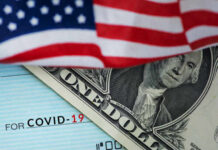 A dollar bill partially covered by an American flag and a COVID-19 stimulus check