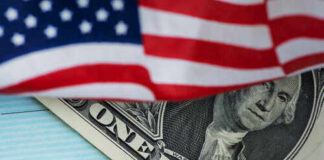 A dollar bill partially covered by an American flag and a COVID-19 stimulus check