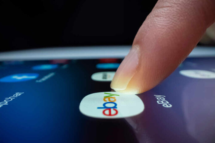 A finger tapping the eBay app icon on a smartphone screen
