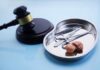 A gavel next to a surgical tray containing medical instruments and an anatomical model