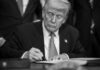 A man in a suit signing a document with a focused expression